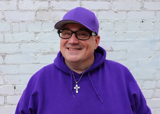 George B. Thomas smiling in a purple hoodie